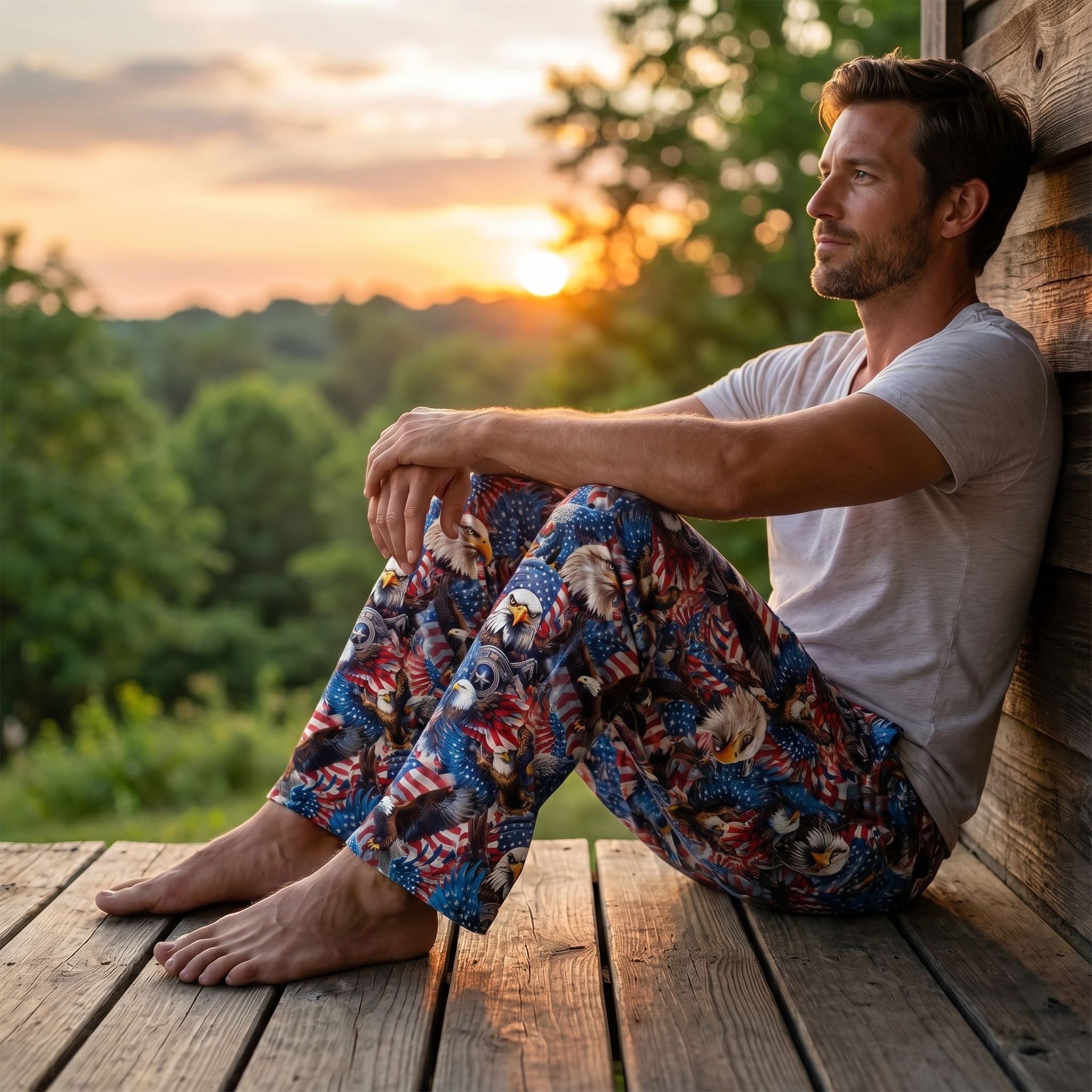 Relaxed male model wearing Eagle Head Flag USA Lounge Pants with patriotic eagle, stars, and waving flags print, sitting on a rustic porch at sunset.