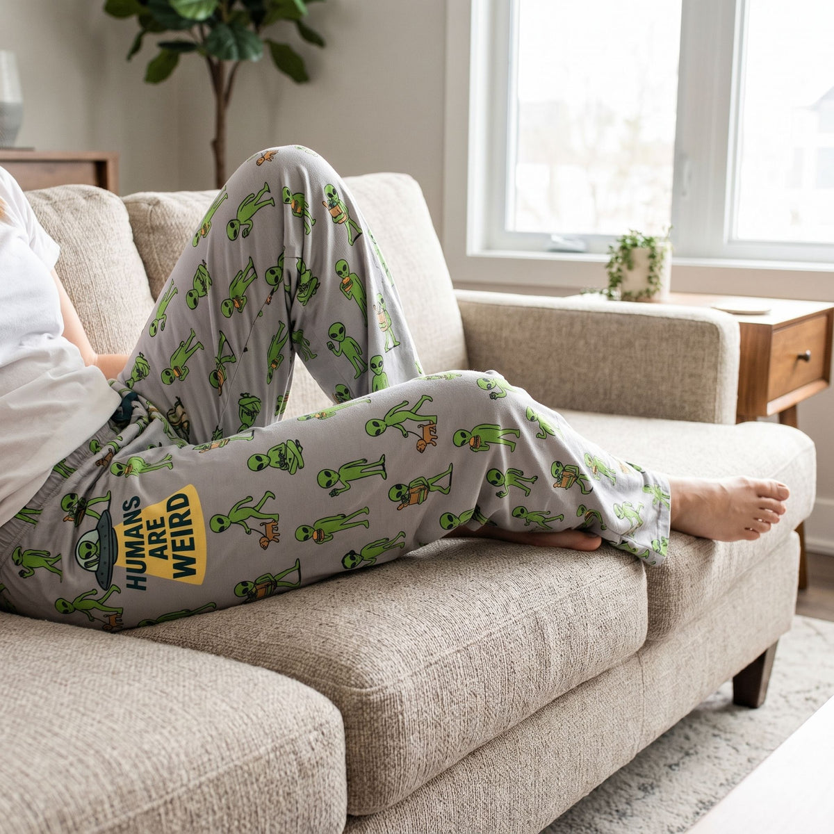 Person wearing gray lounge pants with a playful alien pattern while relaxing on a fabric sofa.