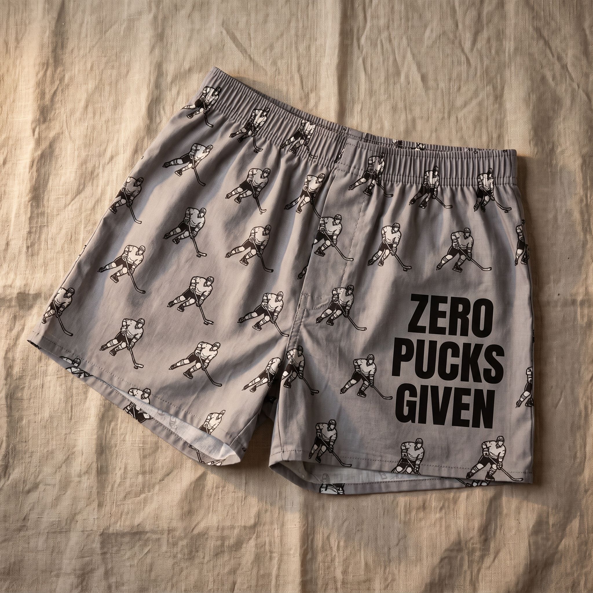 Flat lay of Zero Pucks Given boxer shorts on linen cloth, showcasing pattern, texture, and design details with soft indoor lighting.