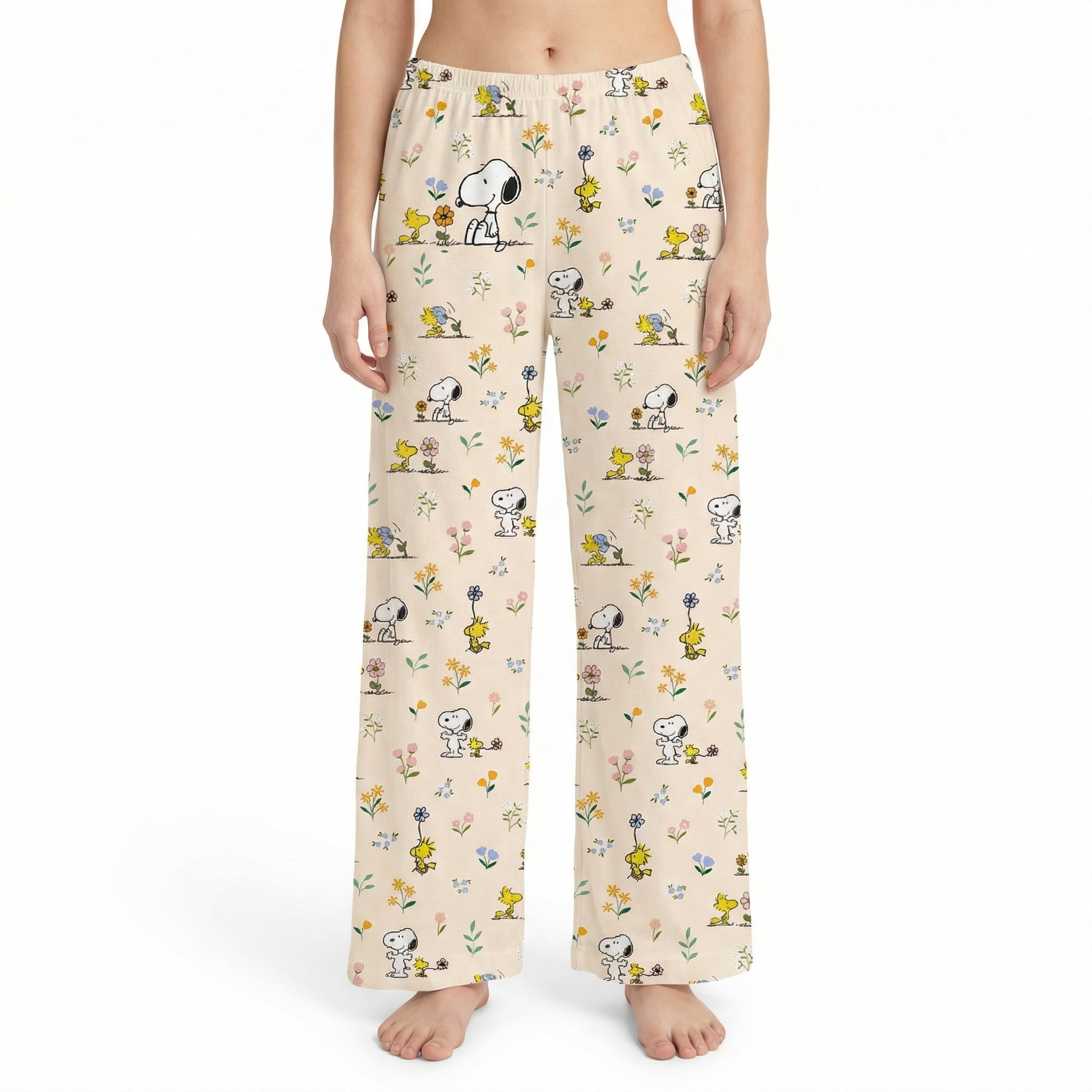 Young female model in Snoopy lounge pants standing in a vibrant, plant-filled living room with colorful decor and natural light.