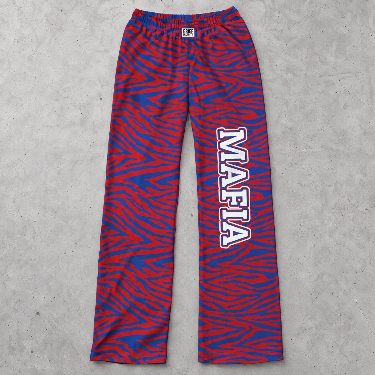Mafia zebra print lounge pants in blue and red laid flat on a gray concrete surface showing knit fabric and elastic waistband.
