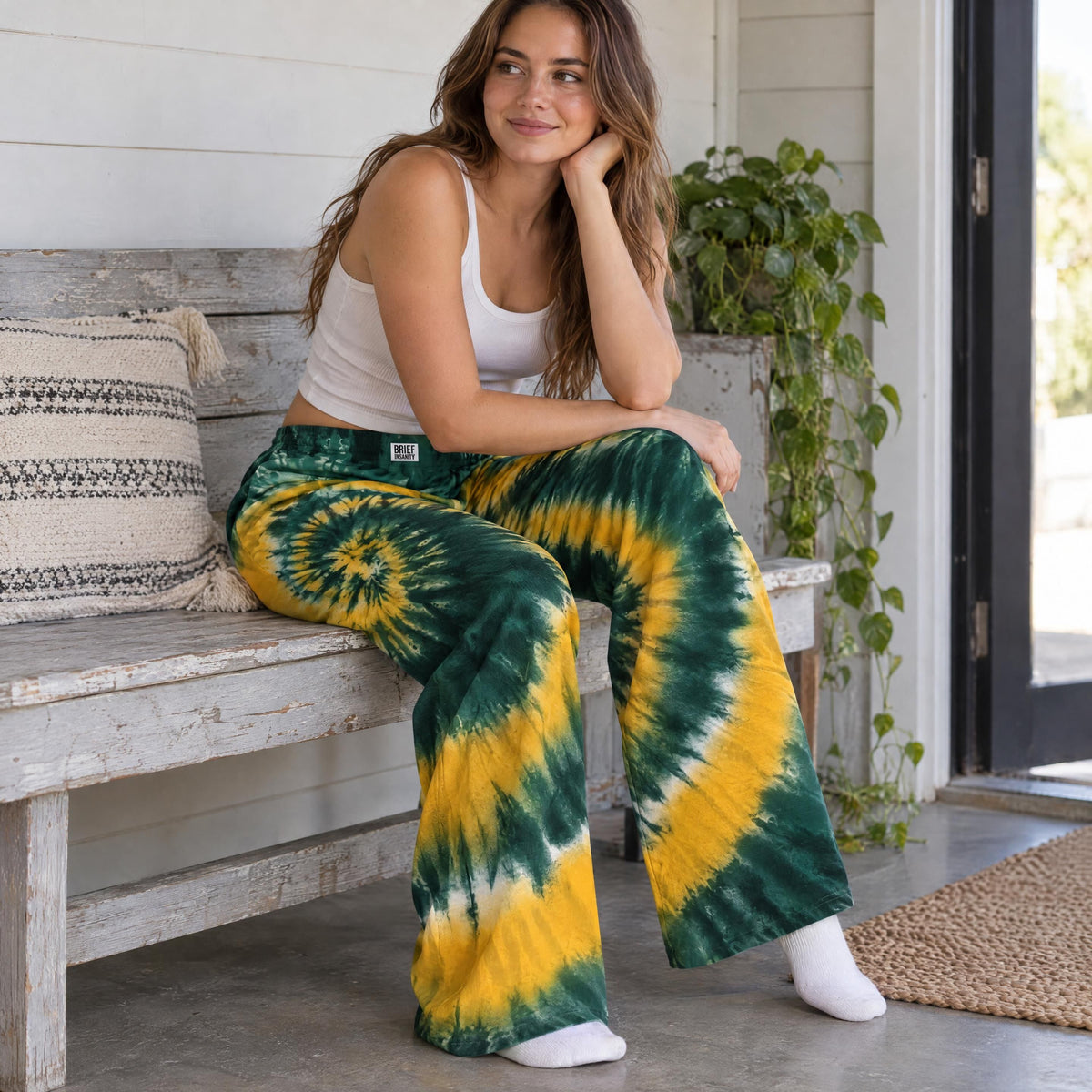 Person sitting on a wooden bench wearing comfortable green and gold tie dye lounge pants with a loose flowing fit.