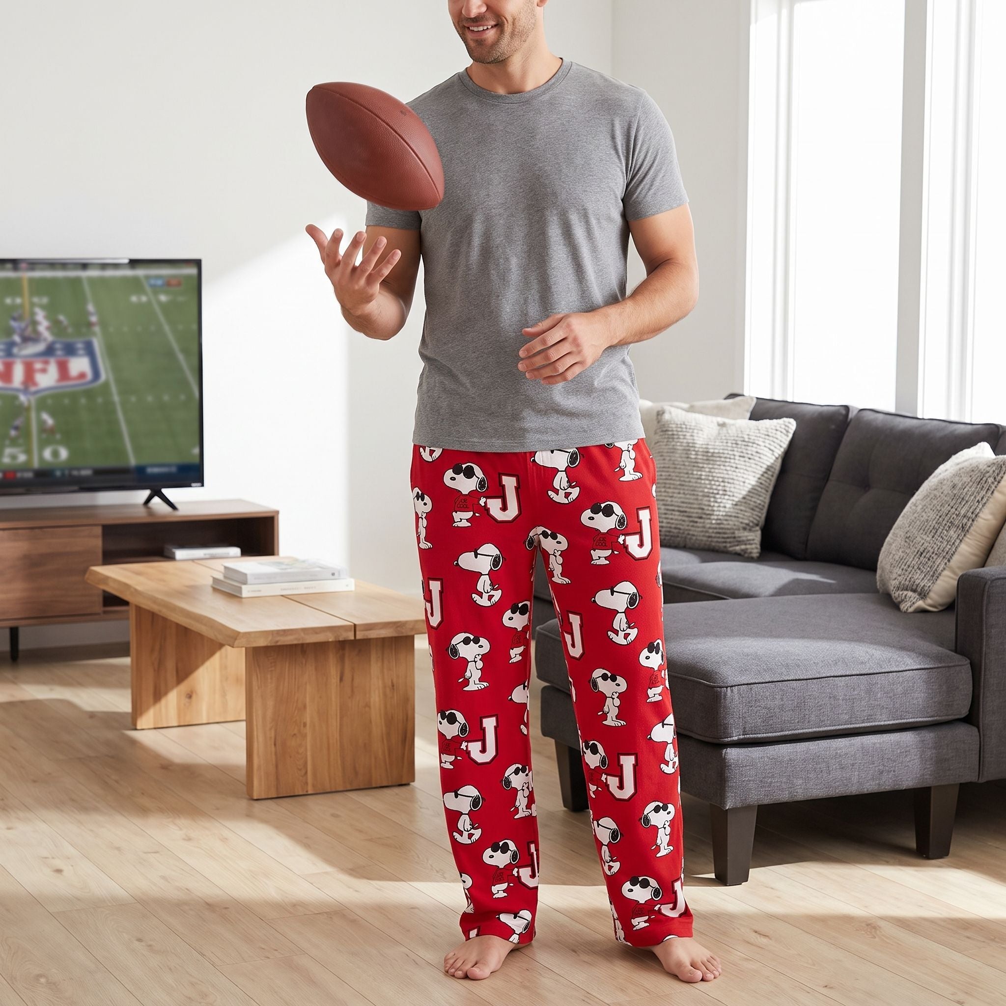 Adult male model wearing red Snoopy Joe Cool lounge pants in a stylish living room during a relaxed game-day afternoon.