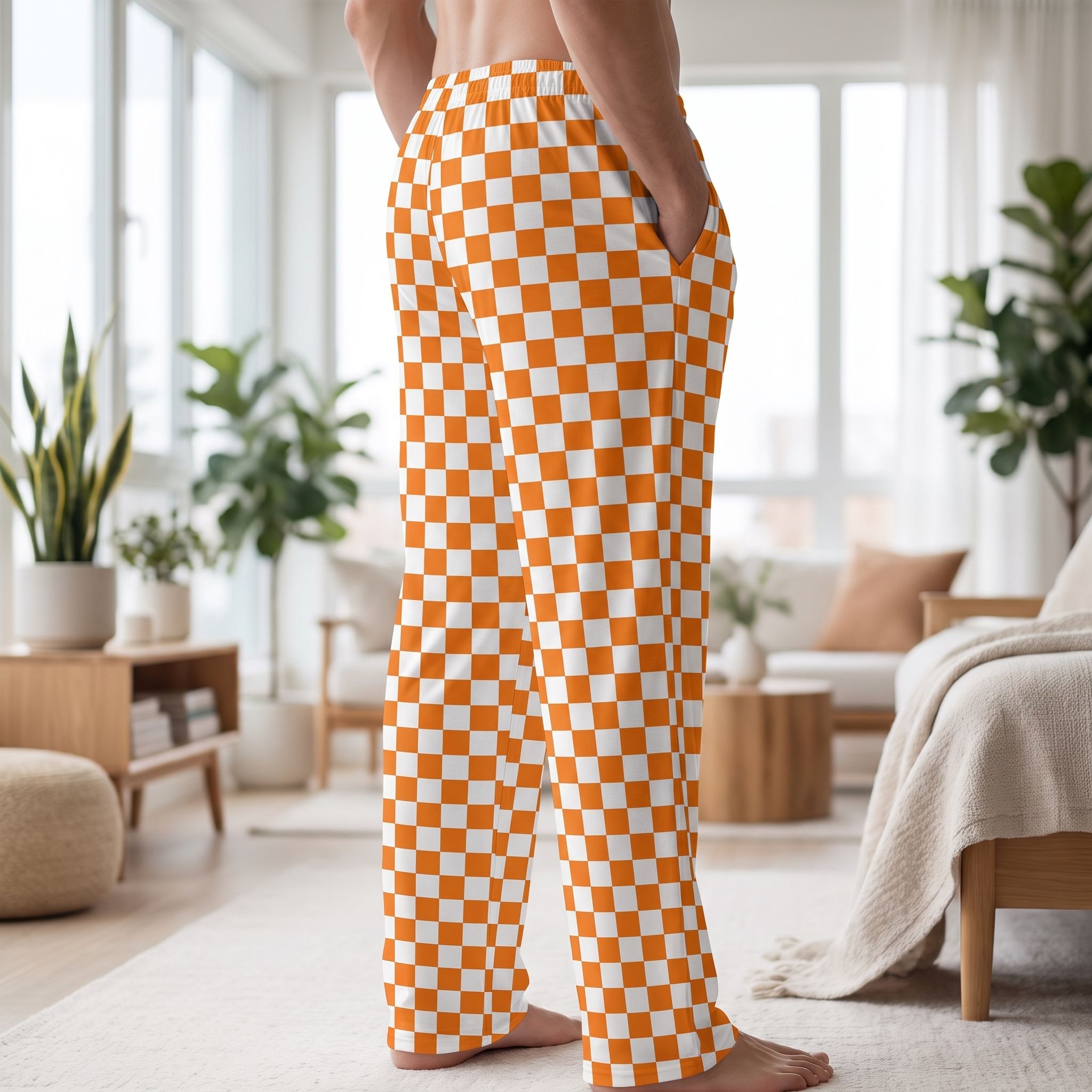 Side view of a model wearing orange checker lounge pants in a bright, airy room, emphasizing the relaxed fit and vibrant pattern.