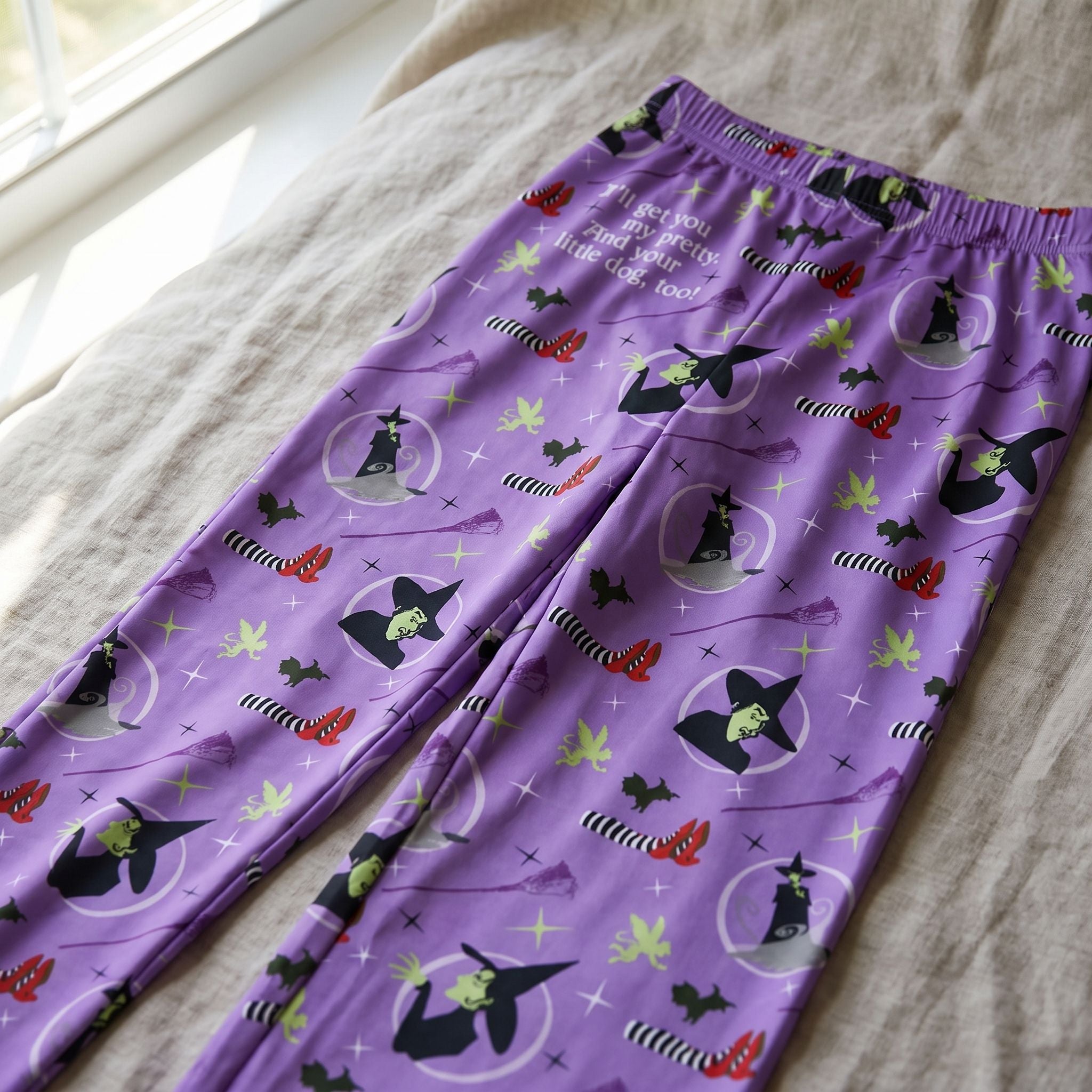 Close-up of Wizard of Oz Wicked Witch lounge pants showing vivid print, smooth fabric texture, and gentle folds on a neutral fabric surface.
