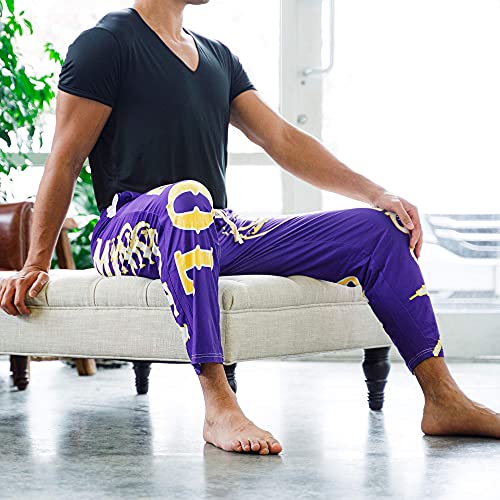 Image of male model sitting on futon wearing SKOL pajama lounge pants (side view)