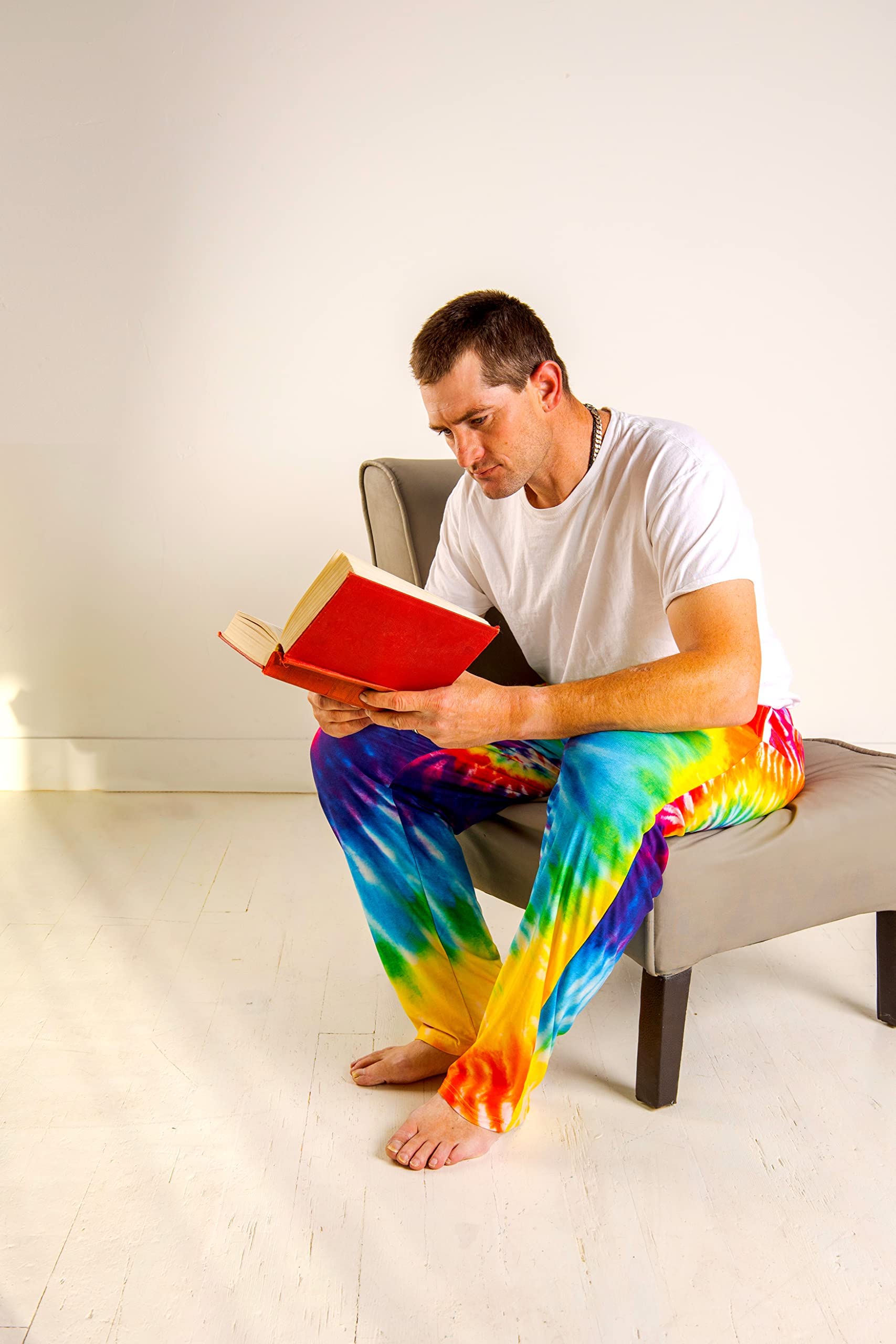 Image of male model sitting on a chair reading a book wearing Rainbow Tie-Dye pajama lounge pants 