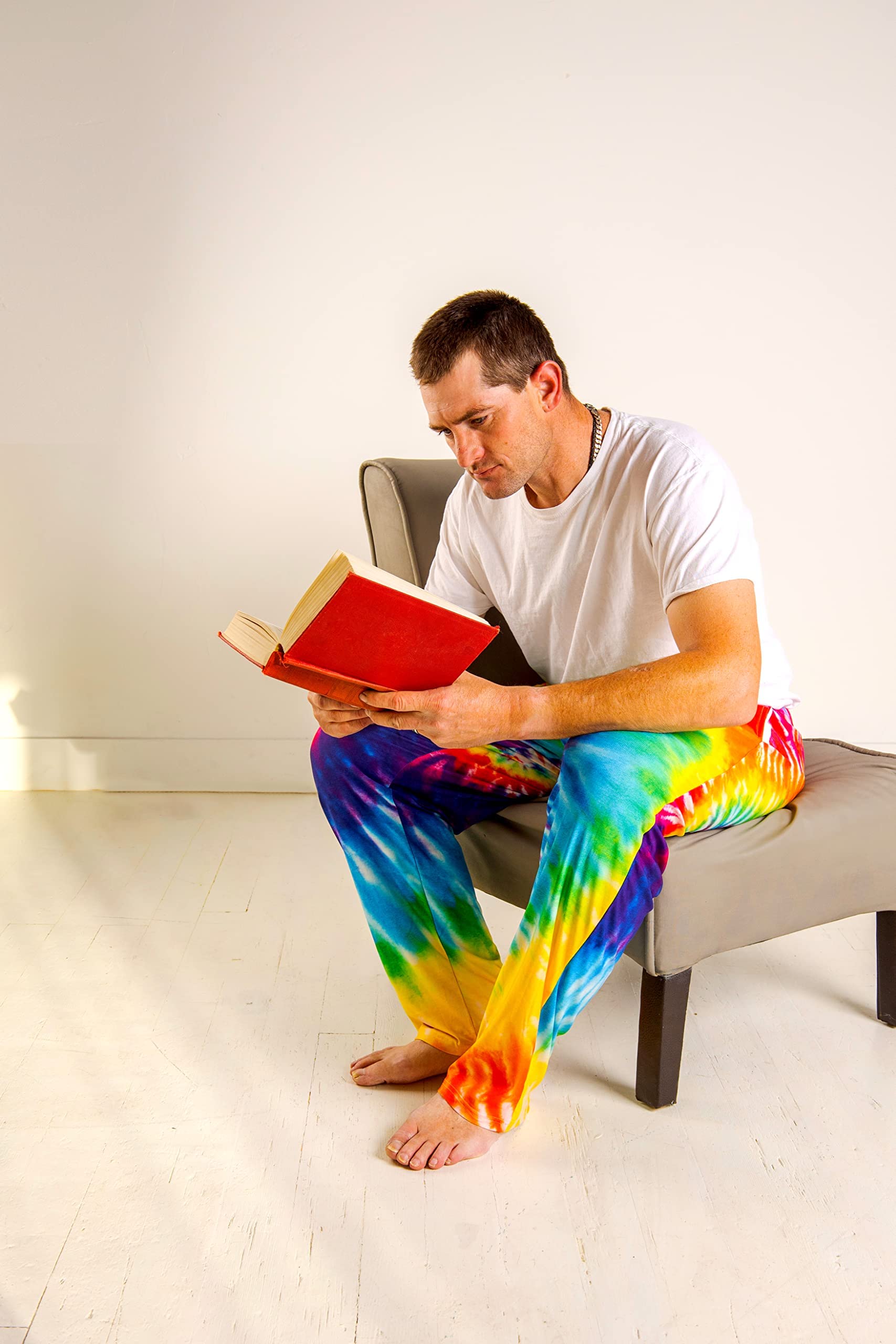 Image of male model sitting on a chair reading a book wearing Rainbow Tie-Dye pajama lounge pants