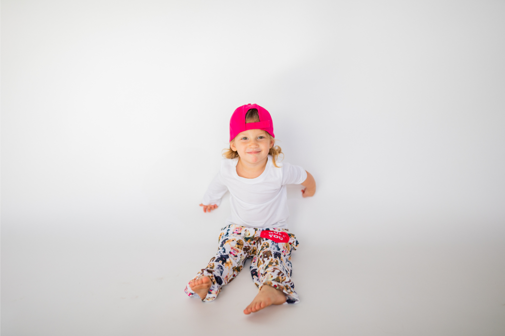 Image of little girl model sitting on floor wearing Ruff Day kids cap backwards (front view white background)