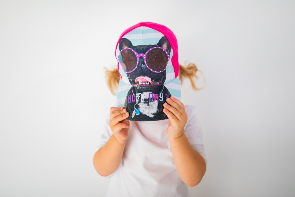 Image of little girl model wearing Ruff Day kids cap and holding it down over head (front view white background)