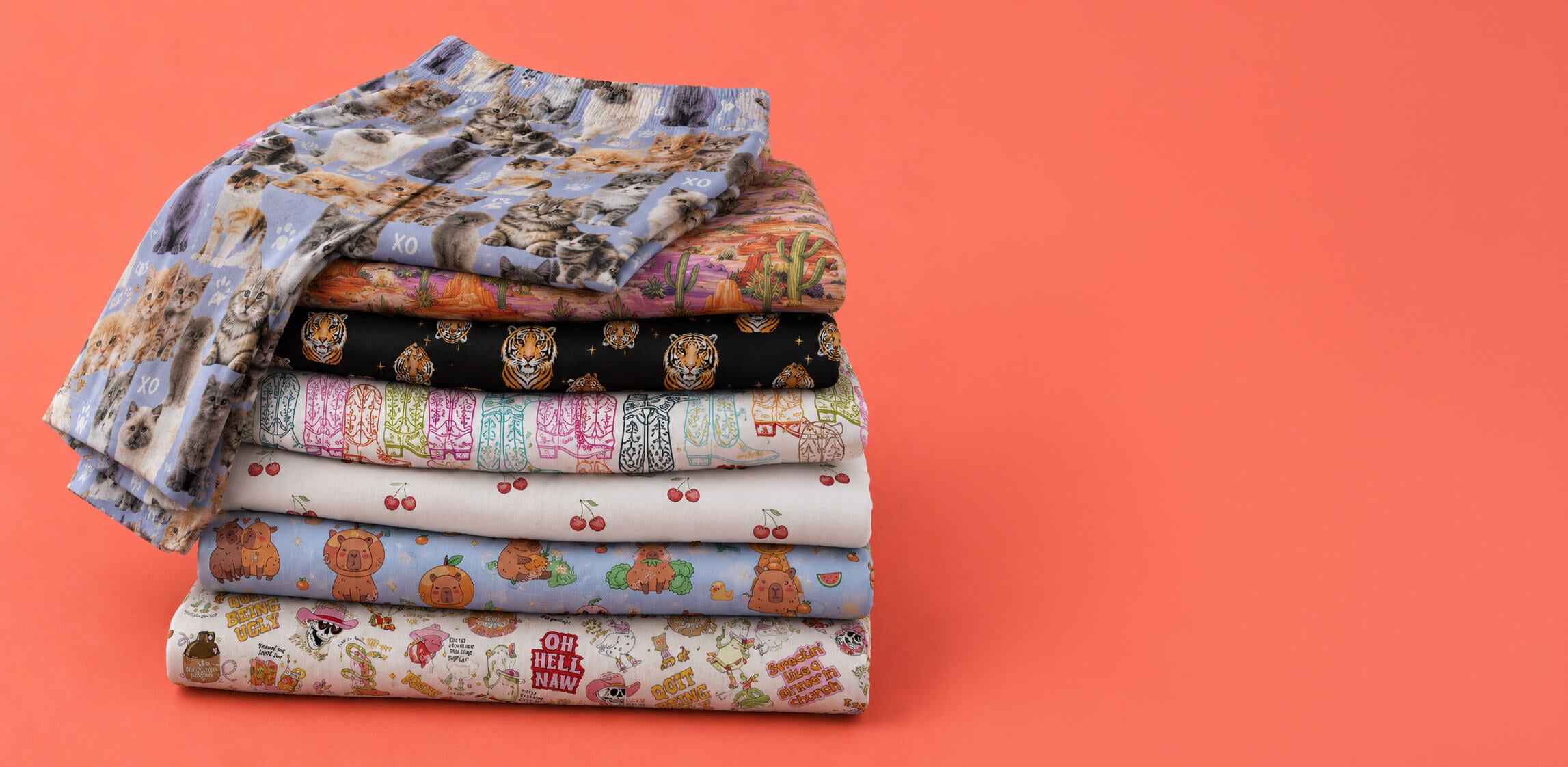 A stack of folded patterned lounge pants in various colors and designs, including floral, cartoon, and striped motifs, set against a solid coral-orange background.