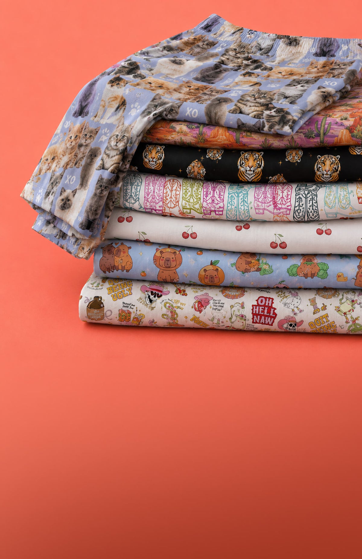 A stack of folded patterned lounge pants in various colors and designs, including floral, cartoon, and striped motifs, set against a solid coral-orange background.
