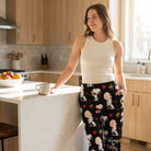 Casual woman wearing Snoopy and hearts lounge pants from the Always & Forever collection, relaxed at home or in a kitchen with morning sunlight.