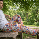 Relaxed model wearing beer-themed lounge pants from Wisconsin sitting on a rustic wooden bench outdoors in a lush green park.