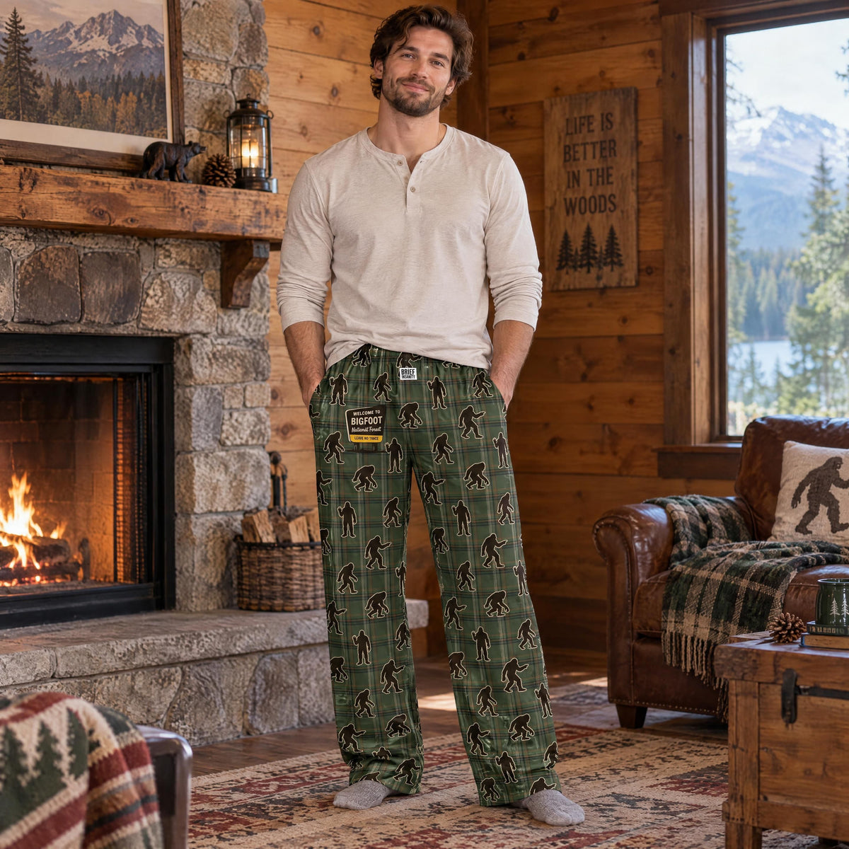 Adult male model wearing Bigfoot plaid lounge pants in a rustic cabin setting.