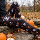 Model seated outdoors on a stone step wearing Boofoot Orange Halloween Lounge Pants with fall leaves and pumpkin background