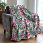 Soft cactus and floral watercolor print throw blanket draped over a charcoal velvet armchair in a bright living room.