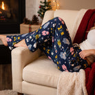 Reclining model styled in Snuggle Weather Lounge Pants with fabric stretch, side pockets, warm ambient lighting, and holiday accents.