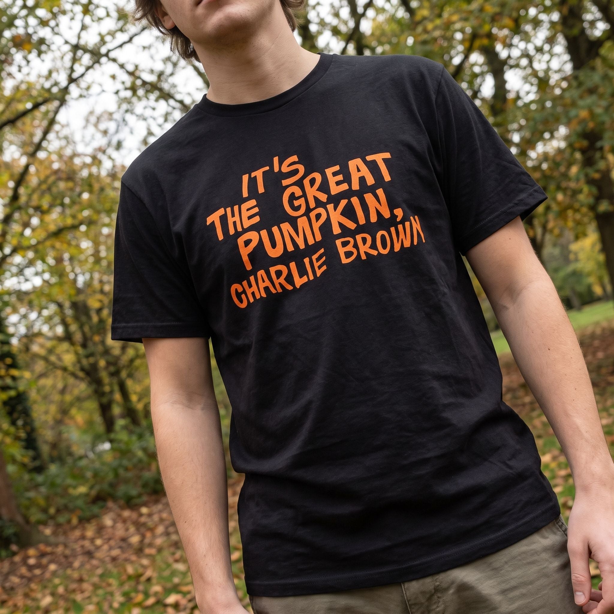 Outdoor scene with a model wearing Charlie Brown Great Pumpkin T-Shirt, featuring natural foliage background and casual style.