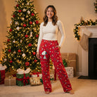 Young adult wearing Snoopy Coco Lounge Pants near decorated Christmas tree in a warmly lit living room, casual pose with soft lighting, holiday ambiance.