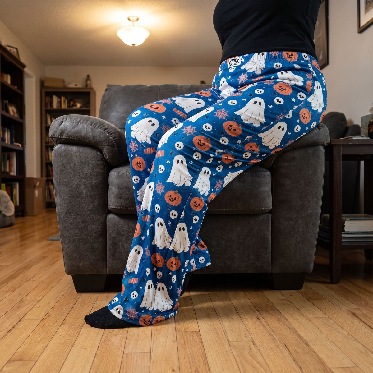 Person sitting on a dark grey armchair wearing blue ghost and candy patterned lounge pants.