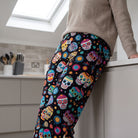 Woman leaning against a kitchen countertop wearing comfortable lounge pants featuring a vibrant Day of the Dead skull print.