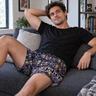 Man lounging on a grey sofa wearing Joker graphic boxer shorts that provide a relaxed and comfortable fit.