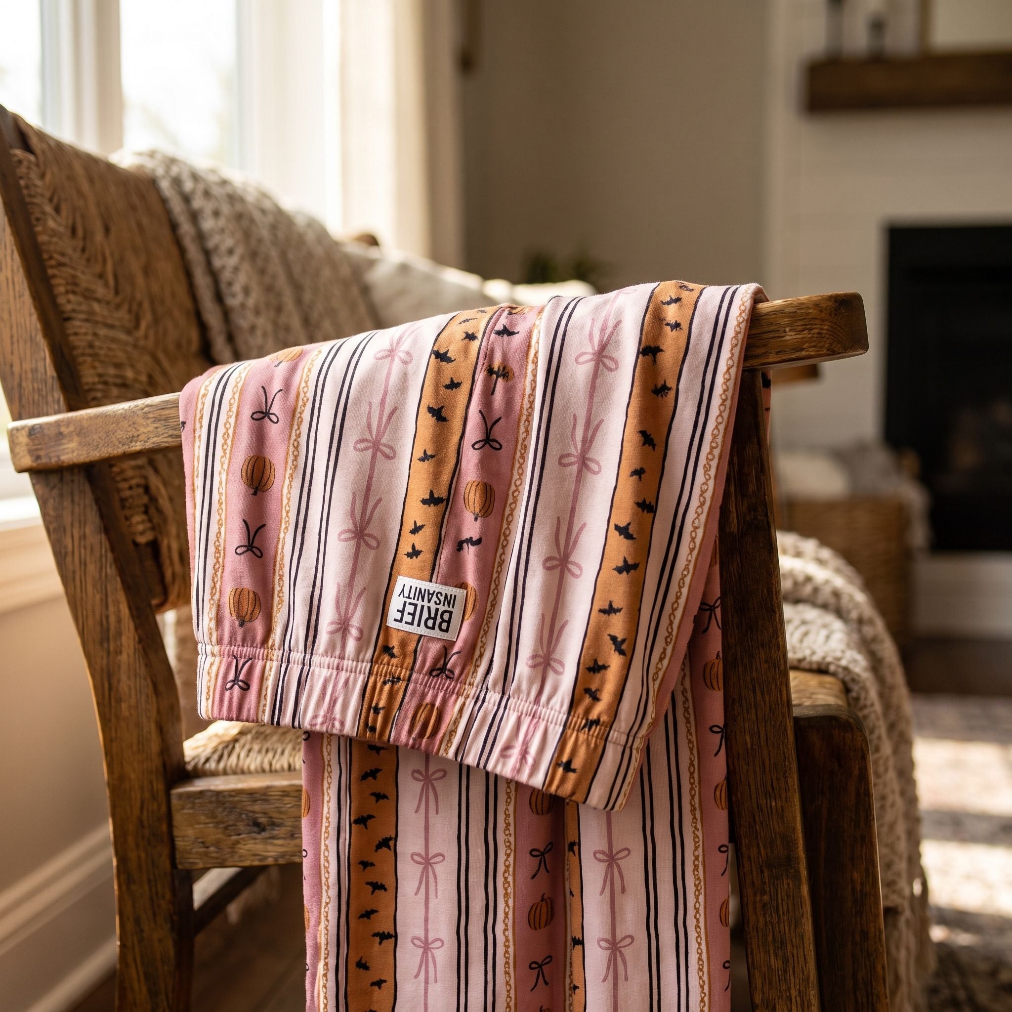 Close-up of Halloween Bows & Stripes lounge pants on a rustic chair, highlighting soft knit fabric with pink bows and pumpkin pattern.