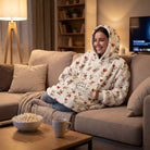 Woman cuddling in oversized blanket hoodie featuring teddy bears, hearts, and balloons during movie night.
