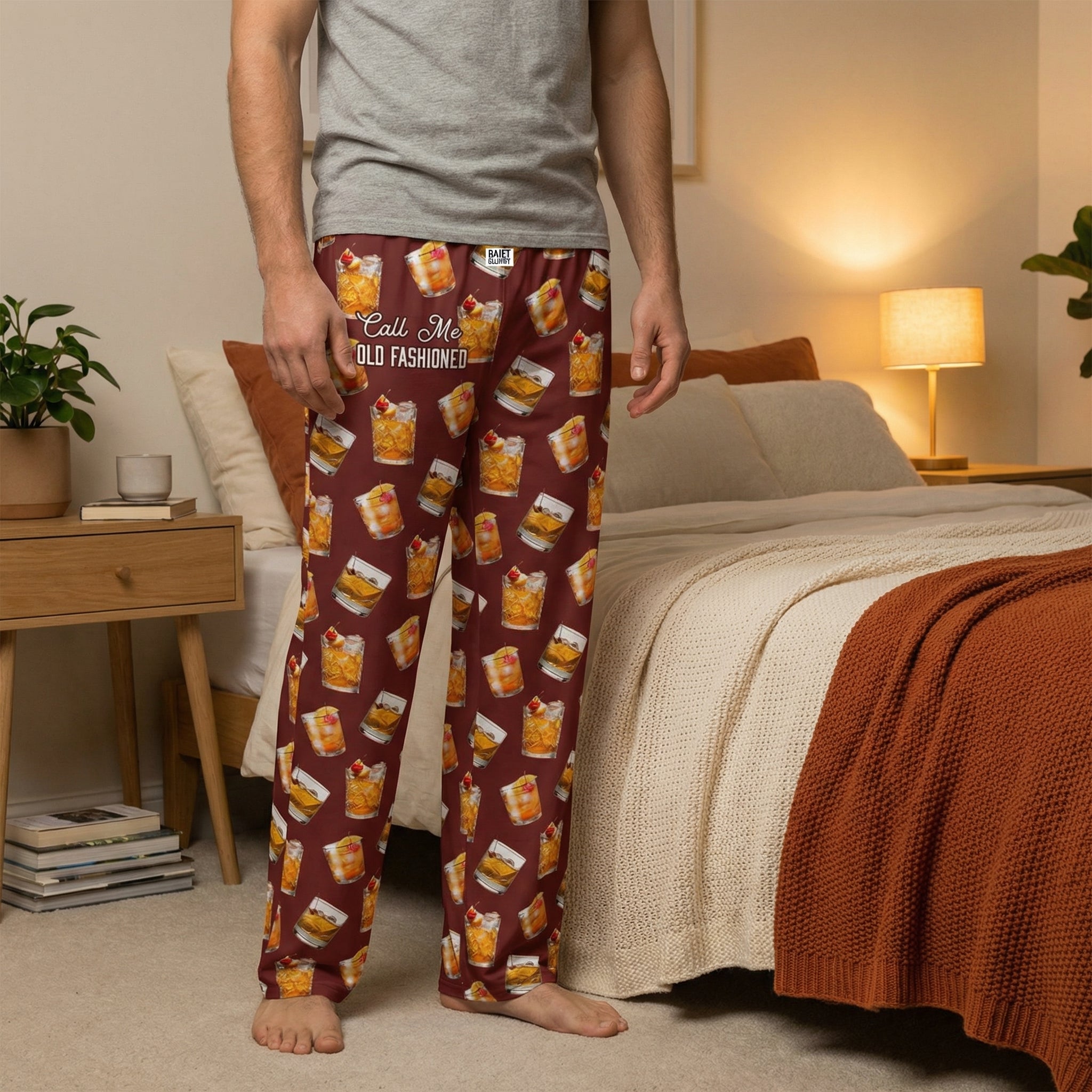 Female model standing in a warm-toned bedroom wearing all-over printed old fashioned lounge pants with cocktails and cheeky phrase, emphasizing comfort and style.