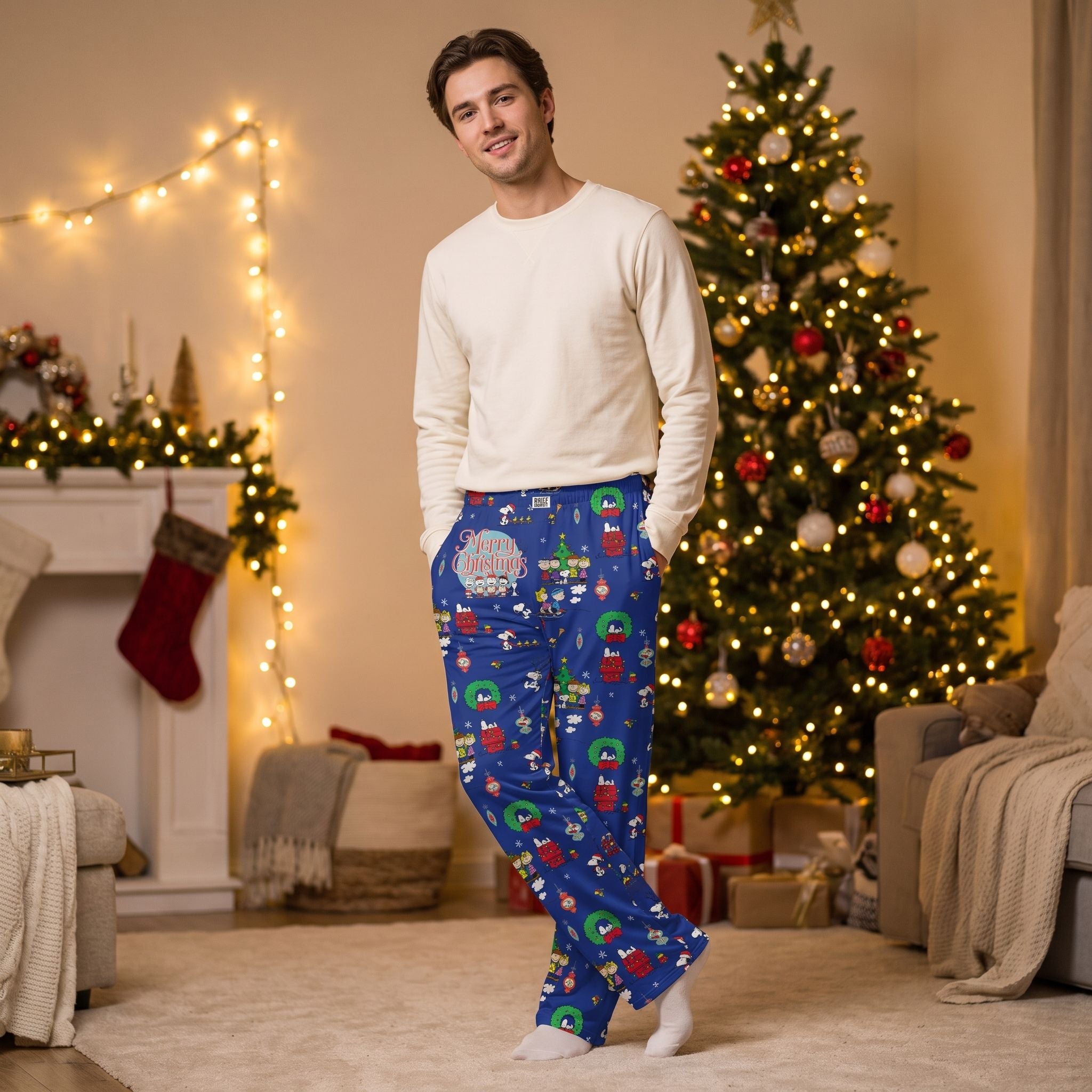 Young male model relaxing in blue Peanuts Christmas lounge pants with holiday decor and soft lighting.