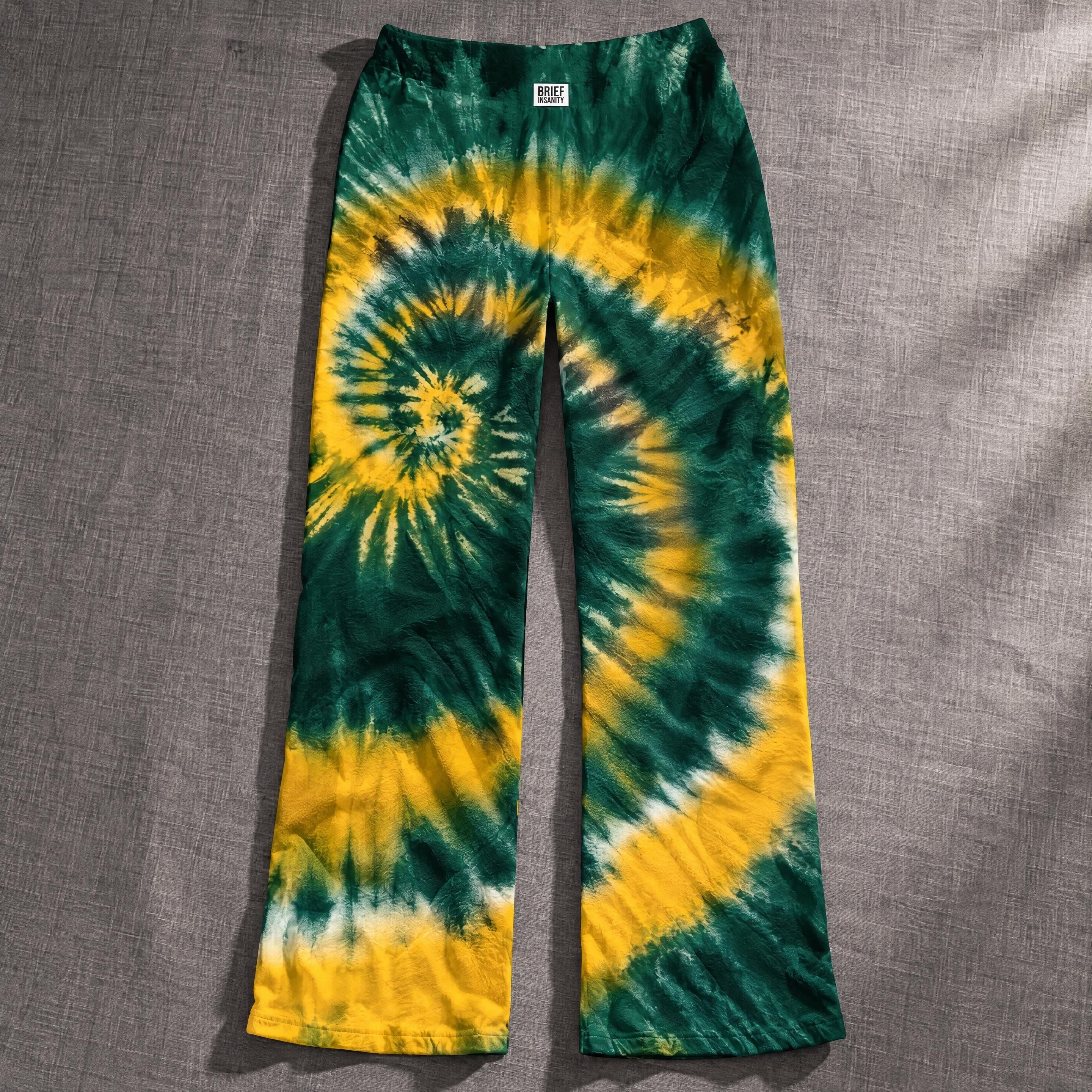Close up of wide leg lounge pants featuring a vibrant green and gold spiral tie dye pattern on lightweight knit fabric.