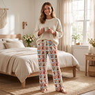 Adult female model in Highland Cow Quilt pajama pants and cream knit sweater, holding coffee in a cozy farmhouse bedroom.