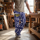 Full-body view of a person wearing blue lounge pants with white tool graphics, relaxed in a cozy workshop setting.
