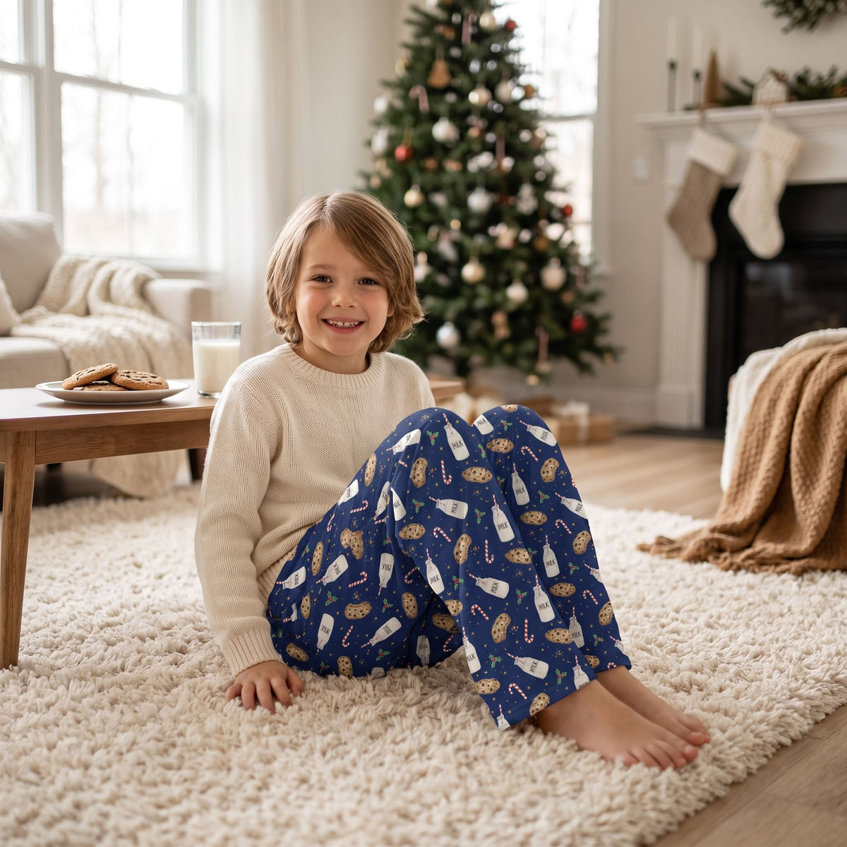 Child modeling kids Christmas blue milk and cookies lounge pants sitting on a plush rug in a cozy home setting.