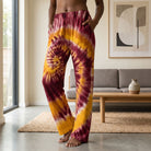 Full-body view of a model wearing maroon and gold tie dye lounge pants in a modern living room, showcasing relaxed fit and vibrant colors.