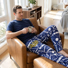 Man relaxing in lounge pants with tool graphics, sitting on a leather recliner with coffee in a bright modern home.