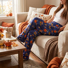 Full-body view of a person relaxing on sofa in Charlie Brown Great Pumpkin Lounge Pants, set in cozy autumn-themed indoor environment.