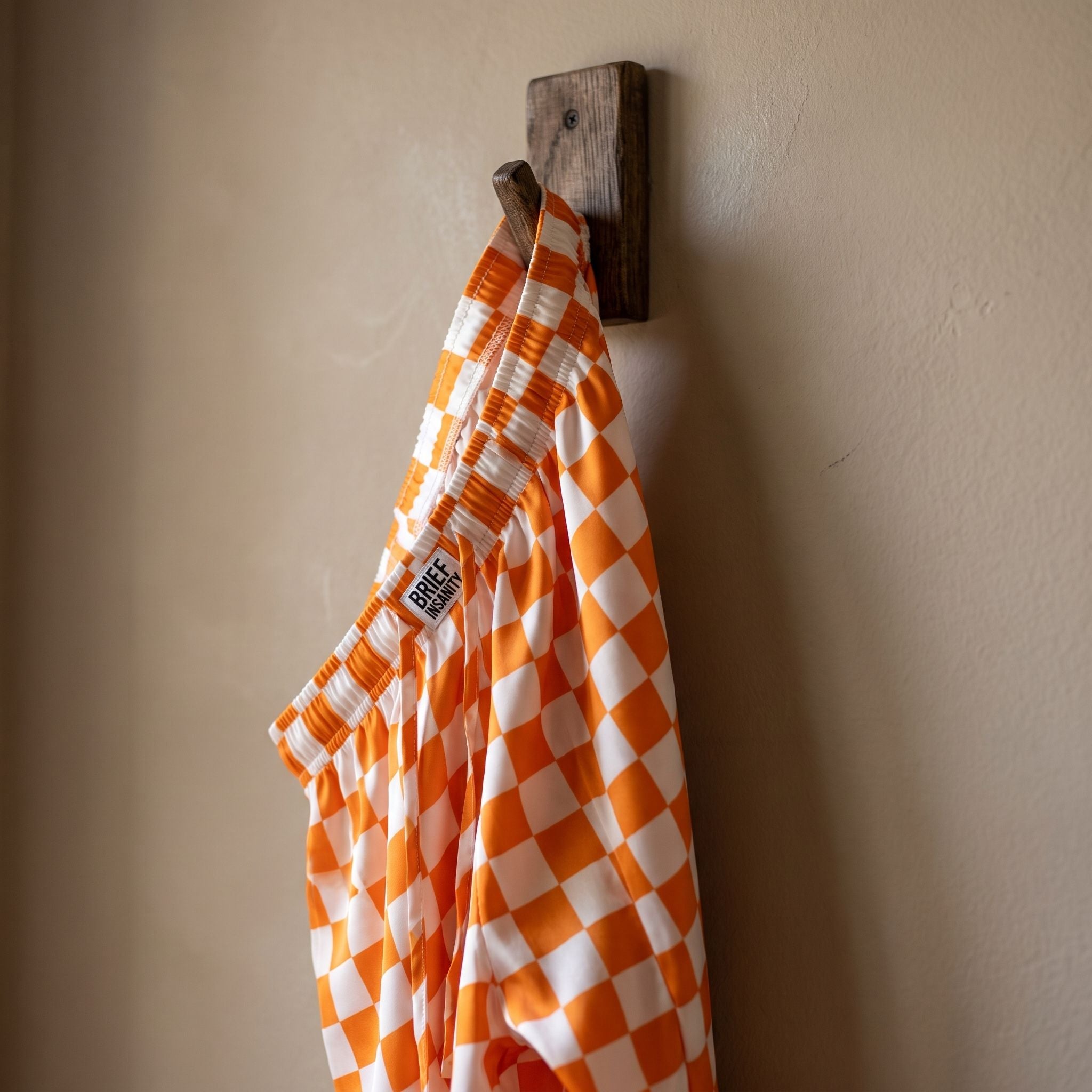 Close-up of orange and white checker lounge pants hanging on a rustic hook, highlighting the vibrant pattern and silky texture.