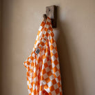 Close-up of orange and white checker lounge pants hanging on a rustic hook, highlighting the vibrant pattern and silky texture.