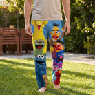 Male model wearing Sesame Street lounge pants, standing outdoors in a sunny backyard with greenery.
