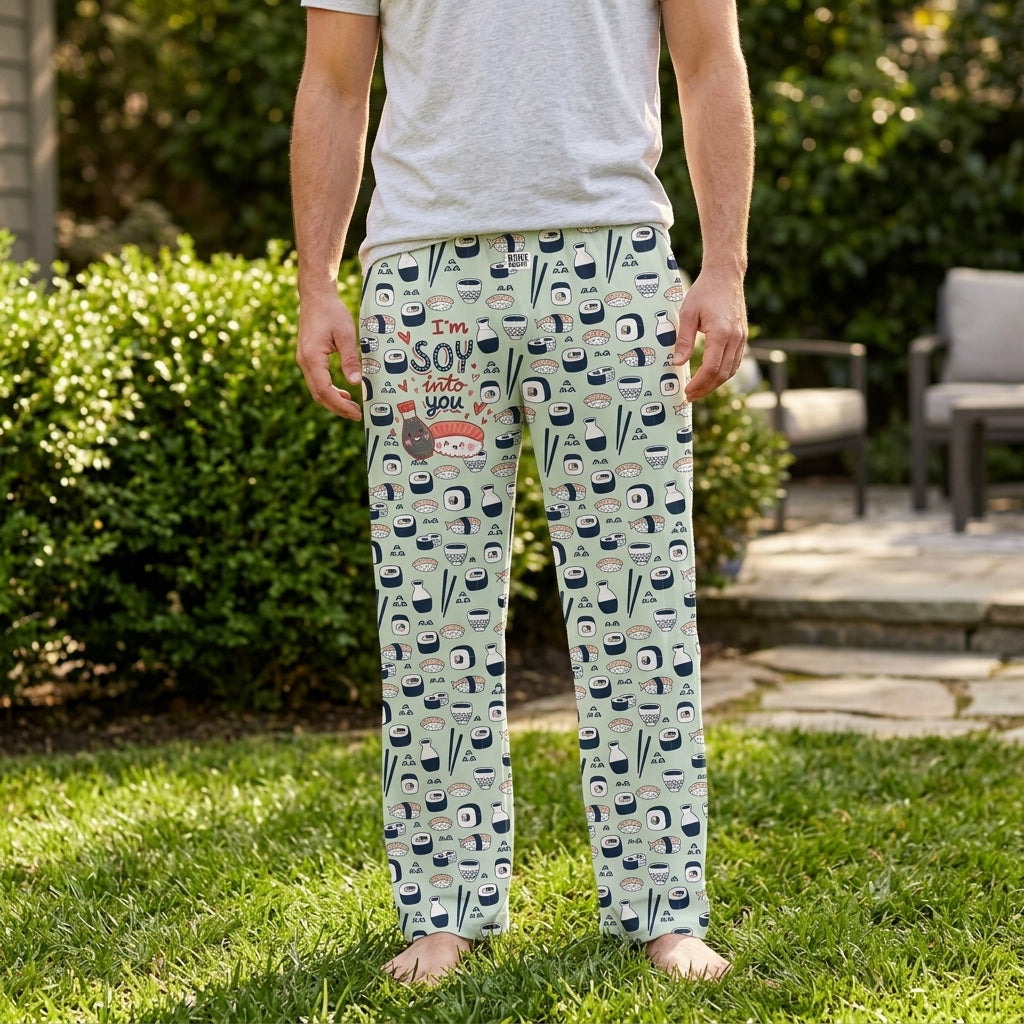 Male model in neutral t-shirt and patterned lounge pants standing outdoors in a sunny backyard with greenery.