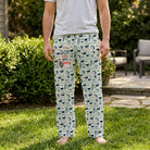 Male model in neutral t-shirt and patterned lounge pants standing outdoors in a sunny backyard with greenery.