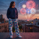 Female model wearing Snoopy Club USA lounge pants and navy sweatshirt on rooftop at dusk with fireworks in the background.