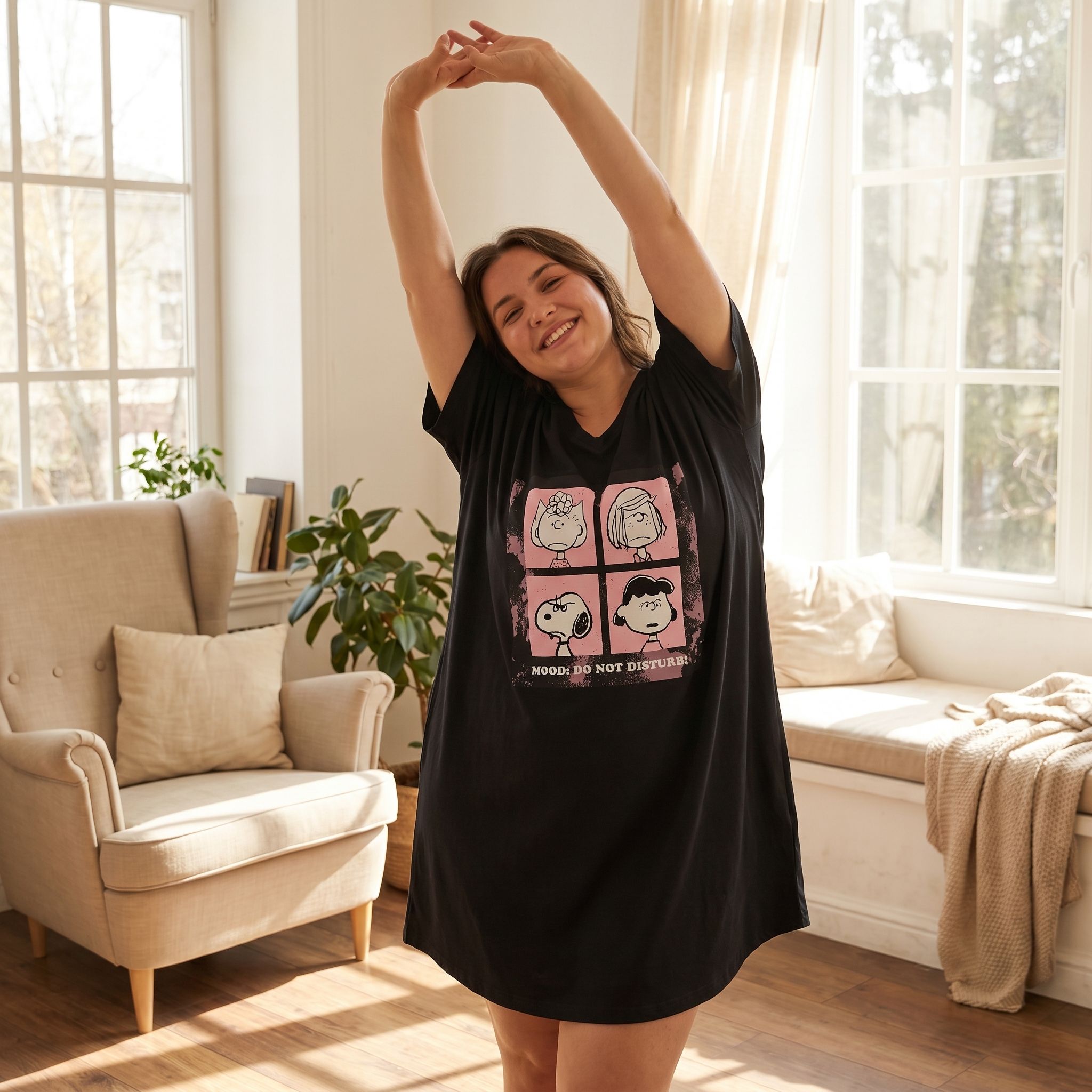 Person stretching and smiling in Peanuts Mood Do Not Disturb Night Shirt, capturing its breathable fabric and relaxed style in a sunlit room.
