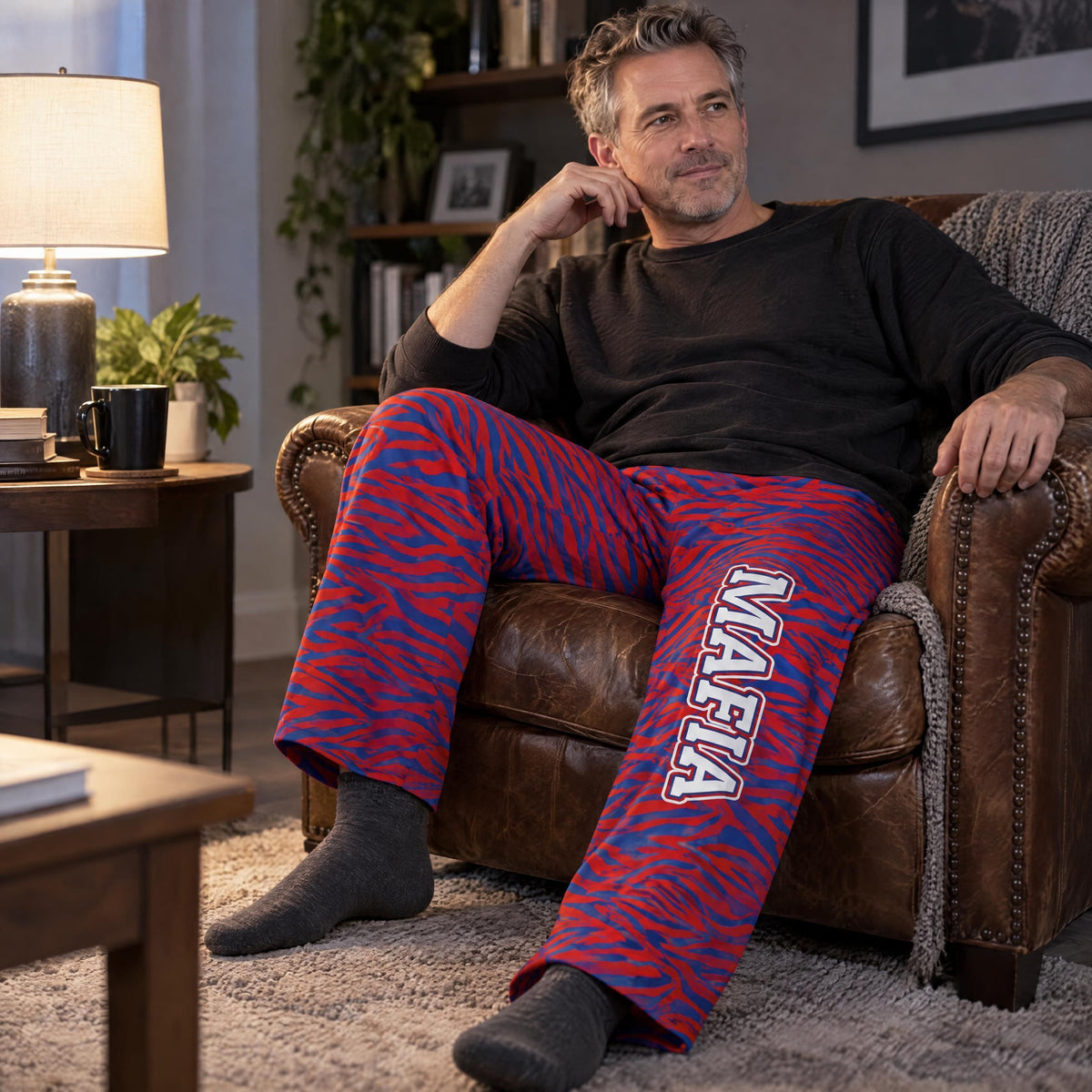 Person wearing blue and red zebra print Mafia lounge pants sitting on a leather chair in a relaxed home setting.