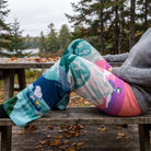 Seated person in Snoopy Cosmic Camping Lounge Pants relaxing on wooden bench outdoor with fallen leaves and overcast daylight.