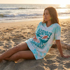 Woman in a modern kitchen wearing the Respect The Locals Night Shirt making coffee, showcasing the soft aqua tie-dye and marine designs.