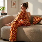Stylish model seated on sofa wearing Pepperoni Lounge Pants, emphasizing fabric texture, sheen, and food-themed decor with cinematic lighting.