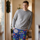 Male model in festive blue Peanuts lounge pants standing near a window with holiday elements and natural daylight.